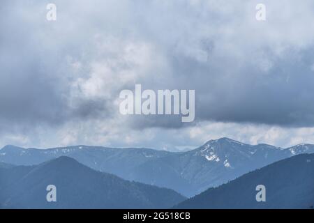 Bellissimo panorama di diverse montagne caucasiche situato sul crinale. Nuvole basse, tempo prima della tempesta in montagna. Silhouette di montagna innevata Foto Stock