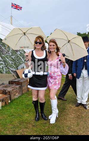 Due donne in stile anni Sessanta vestono sotto ombrelli sotto la pioggia al Goodwood Revival 2012 Foto Stock