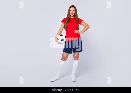 Full length photo positivo allegro calciatore ragazza tenere piede palla pronto giocare mondiale finale campionato torneo di calcio indossare rosso t-shirt blu shorts Foto Stock