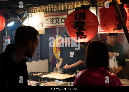 Una donna che fa il takoyaki ad una bancarella di cibo a Dotonbori, Osaka, Giappone Foto Stock