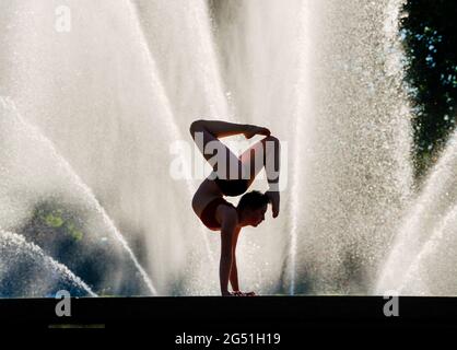 Silhouette di donna che fa il sostegno acrobatico posa contro la fontana Foto Stock