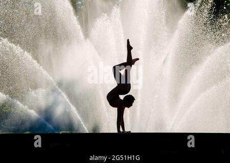 Silhouette di donna che fa il sostegno acrobatico posa contro la fontana Foto Stock