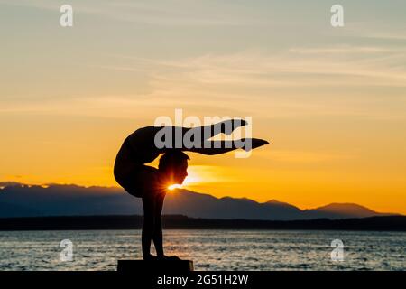 Silhouette di donna che fa il supporto acrobatico posa contro il mare al tramonto Foto Stock