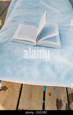c'è un asciugamano e un libro di carta sul molo di legno. Lettura, riposo e relax concetto sulla spiaggia vacanza lettura. Foto Stock