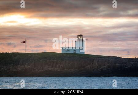 Faro Grand Passage a Brier Island, nuova Scozia, che guida le navi nella Baia di Fundy al tramonto con una bandiera canadese che sventola. Foto Stock