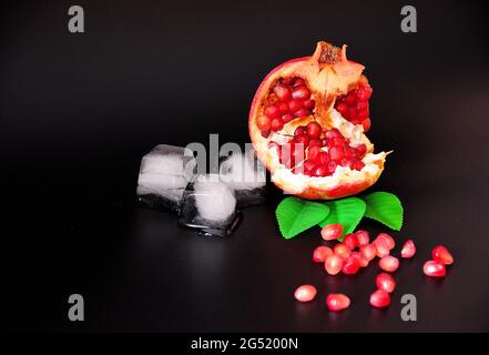 Melograno spezzato maturo con scattering di semi e cubetti di ghiaccio fuso su fondo nero. Primo piano. Foto Stock