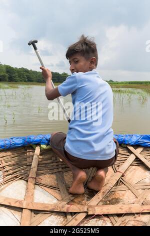 Giovane ragazzo da rurale India canottaggio coracolo, un bambù tradizionale fatto, mentre la pesca in fiume allagato o lago dopo le ore di scuola per l'avventura. Foto Stock