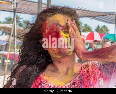 Incredibile foto candida di giovane ragazza che gioca e godendo Holi, festival di colori in India. Applicazione di colori vibranti sul viso a mano e sugli occhi chiusi. Foto Stock