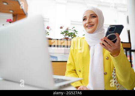 Bella giovane donna musulmana che usa il computer portatile mentre si siede in un bar Foto Stock
