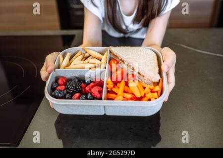 Ragazza irriconoscibile che mostra il pranzo al sacco riempito con cibo sano Foto Stock