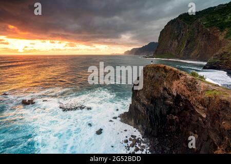 Un uomo che ammira l'alba sull'oceano dalla cima della scogliera, l'isola di Madeira, Portogallo Foto Stock