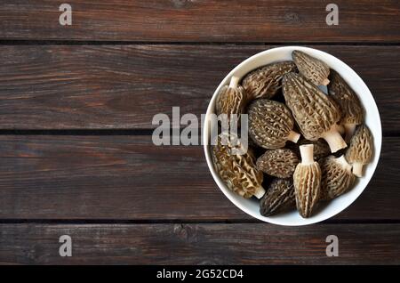 Funghi di spugnole freschi di stagione in una ciotola bianca su un vecchio tavolo di legno con spazio copia, vista dall'alto Foto Stock