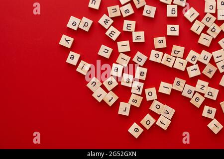 Immagine di sfondo le lettere sono sparse in disordine. Lettere inglesi. Lettere quadrate di legno su sfondo rosso brillante. Biglietto d'auguri, pronto all'uso Foto Stock