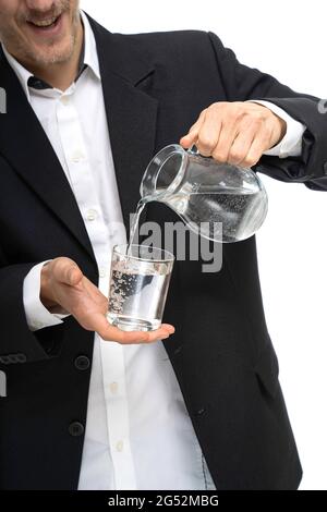 Giovane bell'uomo bianco sottile alto che versa acqua da una caraffa di vetro in nero blazer isolato su sfondo bianco Foto Stock