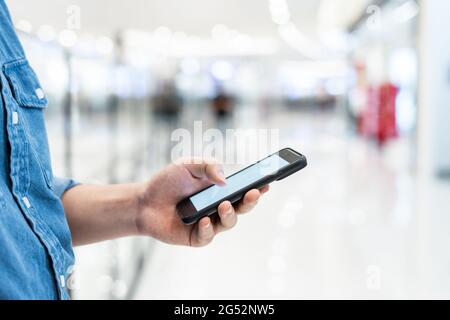 Uomo`s mano che tiene il cellulare smartphone con schermo vuoto a sfondo sfocato centro commerciale. Foto Stock