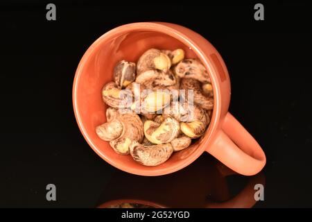 Cashews profumati e salati arrostiti in una tazza di ceramica, primo piano, su fondo nero. Foto Stock