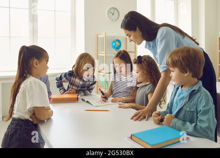 I bambini eseguono compiti sotto la supervisione di un insegnante di scuola materna o di un insegnante di scuola primaria. Foto Stock