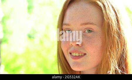 Ritratto una giovane donna sorridente con capelli rossi e fracelle sullo sfondo di un prato luminoso e soleggiato. Bellezza naturale con frettole Foto Stock