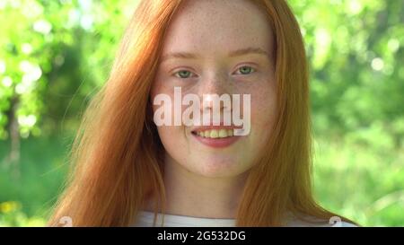 Ritratto una giovane donna sorridente con capelli rossi e fracelle sullo sfondo di un prato luminoso e soleggiato. Bellezza naturale con frettole Foto Stock