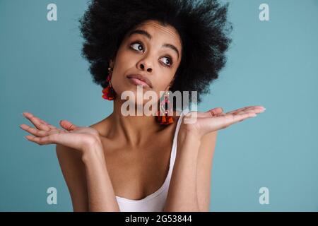 Confusa giovane donna africana shrugging spalle isolate su sfondo blu Foto Stock