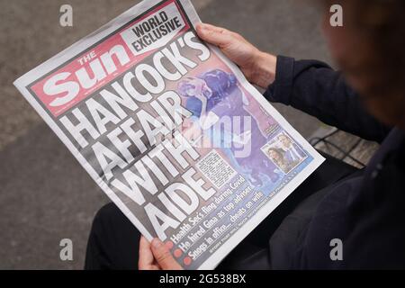 Una persona legge una copia del giornale Sun a Westminster, Londra, con la storia e le immagini del Segretario della Salute Matt Hancock che sembra baciare il suo consigliere Gina Coladangelo, che il giornale ha detto è stato assunto da Hancock l'anno scorso. Data immagine: Venerdì 25 giugno 2021. Foto Stock