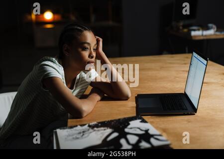 Donna nera stanca che lavora con il computer portatile mentre si siede al tavolo in ufficio Foto Stock