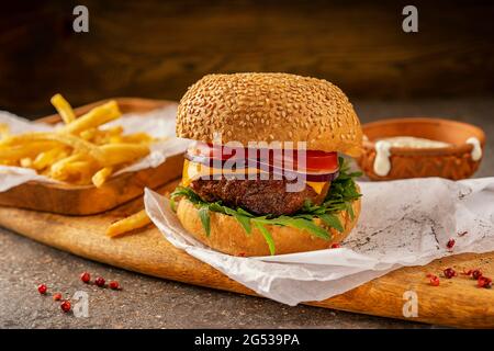 Hamburger e patatine fritte calde pronti a mangiare. Un tagliere fatto di legno di mango in stile rustico. Erbe fresche e insalata di rucola. Godetevi il vostro Foto Stock