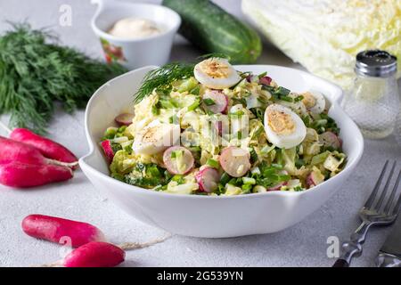 Insalata con cavolo cinese, cetriolo, rafano, cipolle verdi e uova di quaglia in un piatto bianco su sfondo grigio. Foto Stock