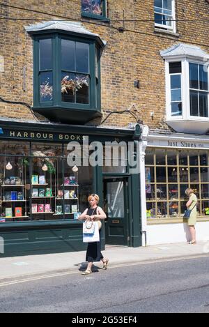 La gente fuori e circa in un sabato soleggiato fuori dai negozi di libri di porto e di Just Shoes in Harbour Street, Whitstable, Kent, Inghilterra, Regno Unito Foto Stock