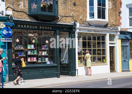 La gente fuori e circa in un sabato soleggiato fuori dai negozi di libri di porto e di Just Shoes in Harbour Street, Whitstable, Kent, Inghilterra, Regno Unito Foto Stock