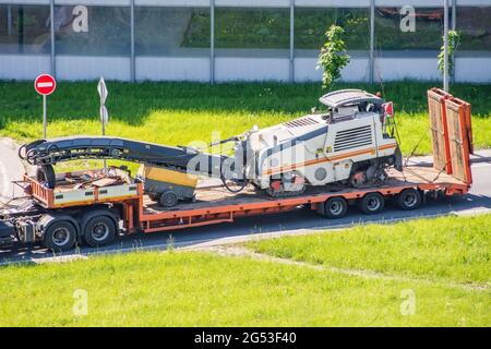 Trasporto di attrezzature per il taglio e la rimozione di vecchie pavimentazioni asfaltate per la riparazione su strada su una piattaforma autocarro di un rimorchio su una strada in un cit Foto Stock