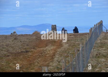 Due uomini che siedono e parlano dallo Stone Tig Point & pile of Stones (Cairn) sulla vetta del Distretto dei Laghi di Wainwright 'Fellbarrow', Cumbria, Regno Unito. Foto Stock