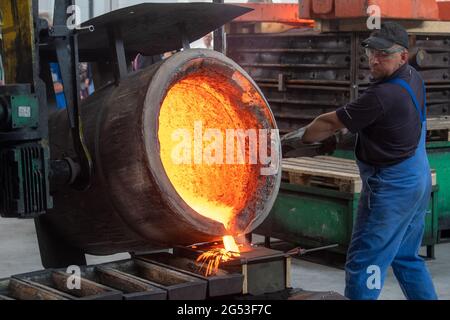 Freiberg, Germania. Giugno 25 2021: Un dipendente del Sächsisches Metallwerk di Friburgo versa un campione di metallo del fuso per una campana per la Cattedrale di Merseburg in una muffa. L'occasione per il lancio della campana è il 1000° anniversario della consacrazione della cattedrale di quest'anno. La campana peserà 890 chilogrammi e suonerà in un unico G. il tono si armonizzerà con le altre campane della cattedrale. Il tono si armonizza con le due grandi campane della chiesa. La campana sarà consacrata il 1° ottobre. La fusione è stata resa possibile da una sovvenzione di 50,000 euro della Friede Springer Foundation. In rosso Foto Stock