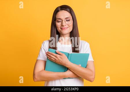 Foto di calma felice donna matura abbraccio libro diario indossare occhiali chiusi occhi godere di storia isolata su sfondo giallo Foto Stock