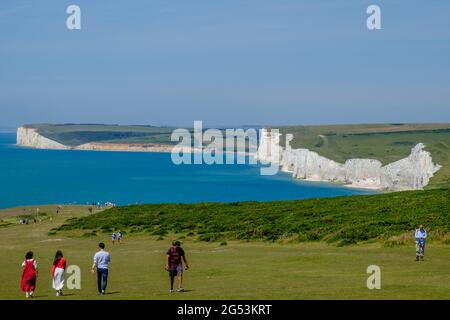 Idea di staycation. Le scogliere costiere di gesso bianco Seven Sisters accanto al canale inglese a Birling Gap, con i turisti che camminano sulla prateria. Foto Stock