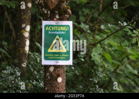 25 giugno 2021, Baviera, Greußenheim: Un segno con l'iscrizione 'attenzione! Pericolo di incendio! - fumo, fuoco e luce aperta sono vietati 'appende su un albero in una foresta. Foto: Karl-Josef Hildenbrand/dpa Foto Stock