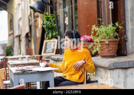 Italia, Toscana, Pistoia, Donna con cuffie sedute in un caffè all'aperto Foto Stock