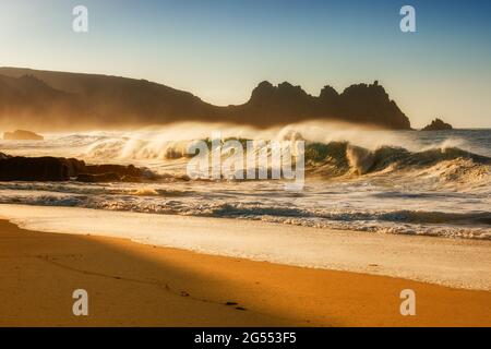 Un'onda che si schiantano sulla spiaggia di Pedrnvounder vicino a Porthcurno in Cornovaglia in una luminosa mattinata estiva.