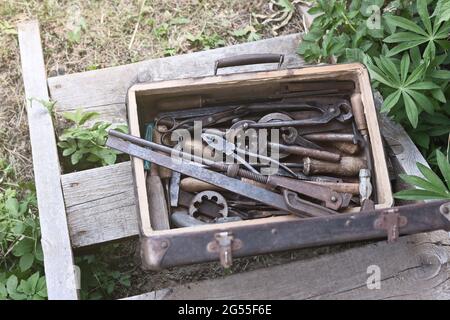 Vari utensili in metallo a mano nella vecchia valigia sulla scala in legno all'aperto Foto Stock