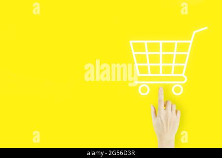 Online shopping business concetto selezione carrello. Mano di giovane donna che punta con ologramma Carrello su sfondo giallo. Digitale Foto Stock