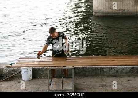 Dnepropetrovsk, Ucraina - 06.21.2021: Un giovane dipinge le tavole sulla riva del fiume. Foto Stock