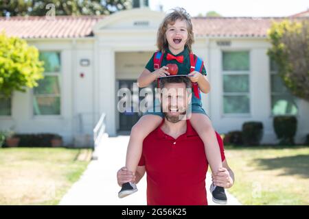 Genitore e bambino stupito piggyback vicino a scuola. Scolaro che va a scuola con il padre. Foto Stock