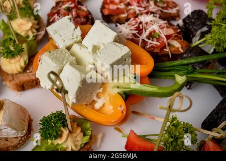 Pezzi tritati di formaggio greco turco feta messi sul pepe e serviti sul tavolo. Buffet per gli ospiti. Vassoio con deliziosi formaggi Foto Stock