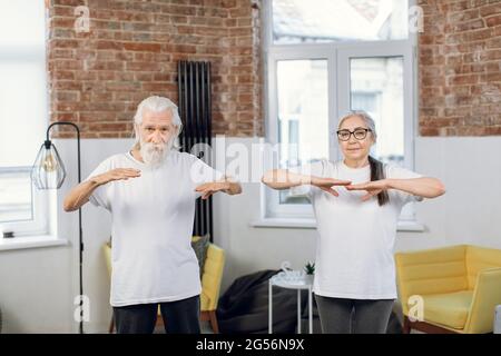 Vista frontale della coppia matura in allenamento di activewear insieme in un luminoso soggiorno. Felice uomo e donna di età che conduce uno stile di vita attivo e sano in pensione. Foto Stock