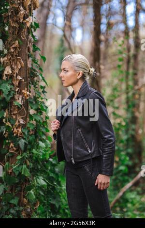 Moda in luoghi insoliti, giovane donna in giacca Edgy Moto nella foresta Foto Stock