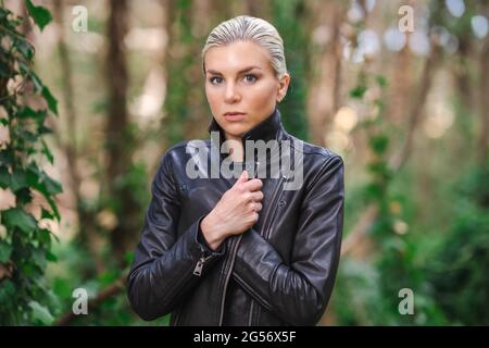 Moda in luoghi insoliti, giovane donna in giacca Edgy Moto nella foresta Foto Stock