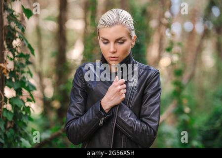 Moda in luoghi insoliti, giovane donna in giacca Edgy Moto nella foresta Foto Stock