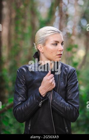 Moda in luoghi insoliti, giovane donna in giacca Edgy Moto nella foresta Foto Stock