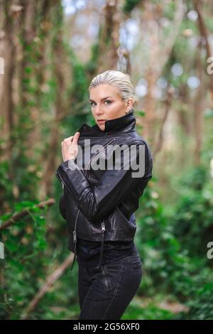 Moda in luoghi insoliti, giovane donna in giacca Edgy Moto nella foresta Foto Stock