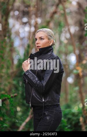 Moda in luoghi insoliti, giovane donna in giacca Edgy Moto nella foresta Foto Stock